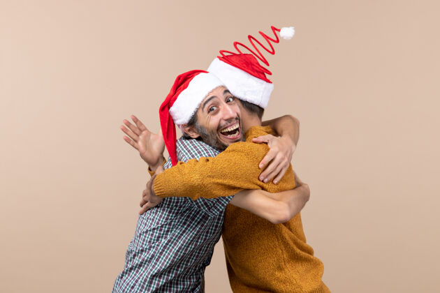 微笑前视图两个微笑的家伙与圣诞帽拥抱对方米色孤立的背景肖像视图圣诞老人