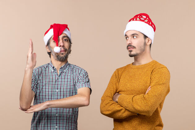 男人前视图两个圣诞节的家伙一个举起他的手 另一个在米色孤立的背景笑前面伙计们米色