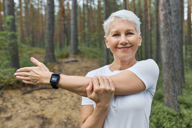 慢跑短发退休女性的肖像 穿着白色t恤 手腕上戴着智能手表 在跑步过程中跟踪进度成人乡村运动