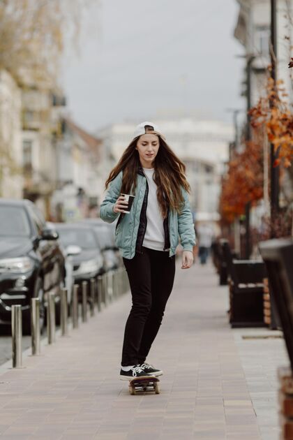 年轻溜冰的女孩一边溜冰一边拿着一杯咖啡城市生活城市