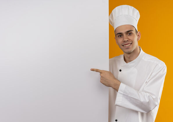 穿笑容可掬的男青年酷穿厨师制服 手指指向白墙与临摹空间墙手指酷
