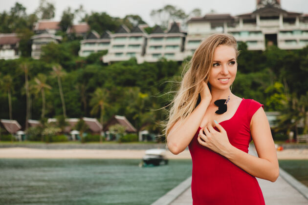 海洋年轻漂亮迷人的女人独自站在豪华度假酒店的码头上 暑假 红色长裙 金色头发 性感服装 热带沙滩 诱惑 性感 微笑人魅力放松