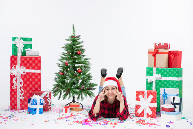 周围正面图：年轻女性躺在圣诞礼物和白色背景上的小圣诞树旁寒冷的女人圣诞节新年下雪礼物雪树