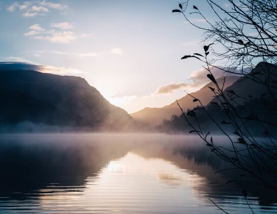 雾美丽的湖景被群山环绕 背景是灿烂的太阳雾景色发光