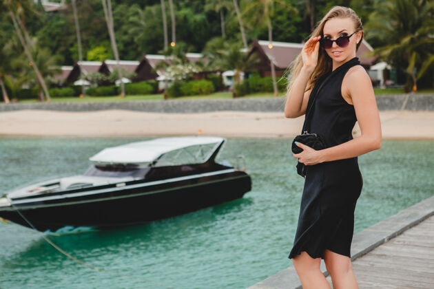 帆船奢华性感迷人的女人穿着黑色礼服在豪华度假酒店的码头上摆造型 戴着墨镜 暑假 热带海滩女孩女士服装