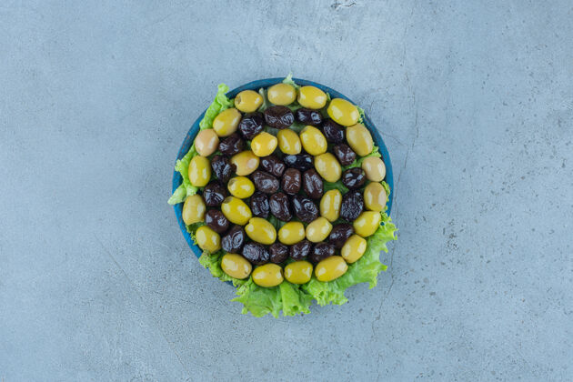 莴苣无髓橄榄放在莴苣覆盖的大盘上 放在大理石上拼盘顶视图橄榄