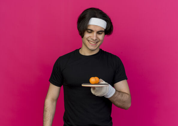 积极年轻的运动型男子穿着运动服 戴着头巾 手持球拍和乒乓球 微笑着快乐和积极站着年轻桌子