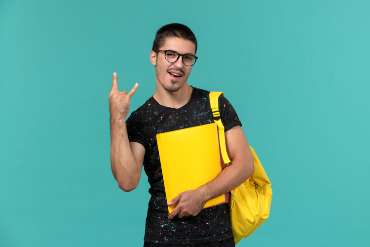 男学生身穿深色t恤黄色背包的男生正面图 浅蓝色的墙上放着不同的文件教训黑暗背包