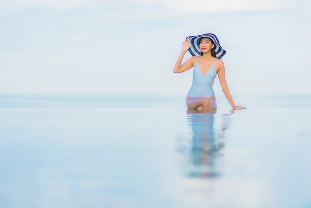 度假村肖像美丽的亚洲年轻女子放松微笑周围的室外游泳池在酒店度假村太阳镜水游泳池