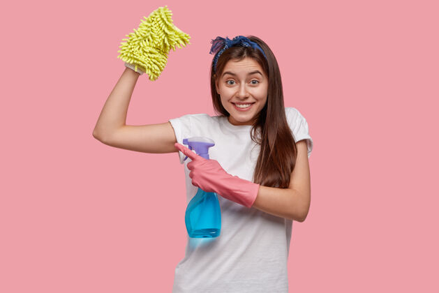 家务积极的年轻女子在疲惫的工作后展示肌肉 穿着白色休闲t恤 拿着一瓶喷雾女佣洗涤T恤