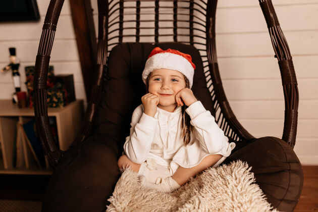 季节快乐的小女孩穿着圣诞老人的服装在家里摆姿势等待圣诞礼物女孩快乐房间