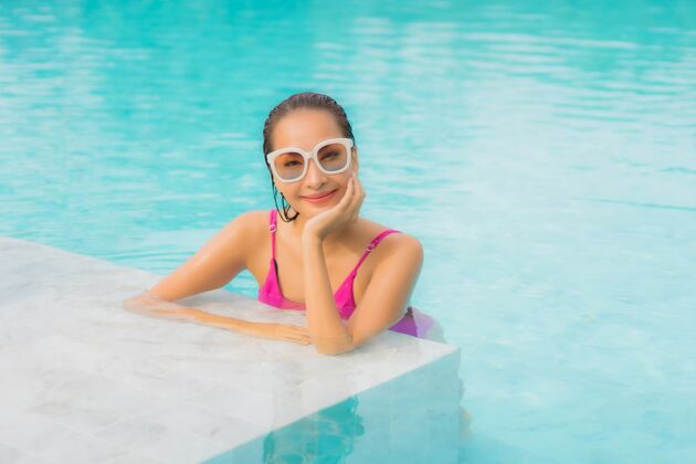 度假村肖像美丽的亚洲年轻女子放松微笑周围的室外游泳池在酒店度假村比基尼游泳帽子