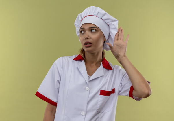 厨师看着旁边穿着厨师制服的年轻厨师女在隔离的绿色墙壁上展示倾听的手势 还有复制空间制服手势年轻