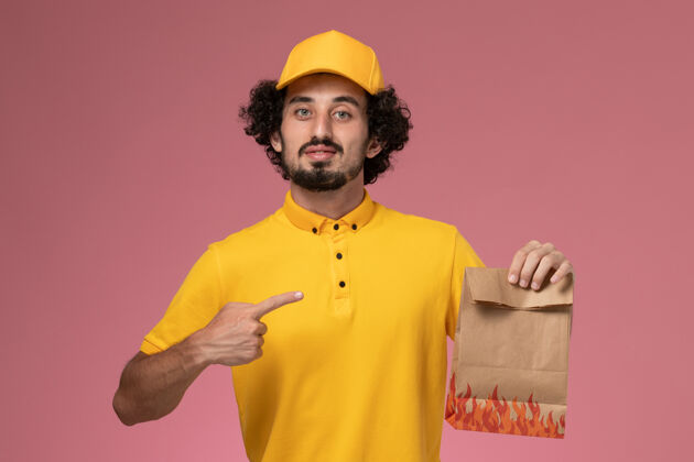 黄色正面图穿着黄色制服的男快递员拿着浅粉色墙上的纸质食品包服务持有视野
