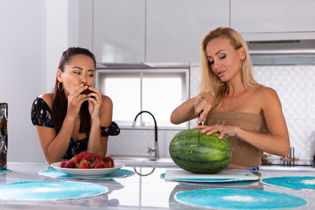 聊天两个女朋友在厨房吃西瓜和红毛丹热带水果现代水果烹饪