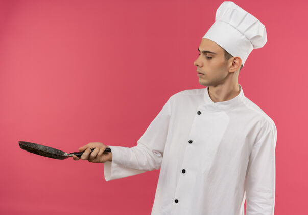 厨师站在剖面图年轻的男厨师穿着厨师制服看着煎锅与复制空间制服穿煎