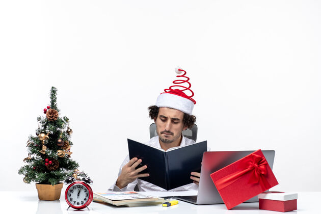 专业困惑的年轻商人 戴着滑稽的圣诞老人帽子 在白色背景的办公室里查看文件中的信息人年轻电脑