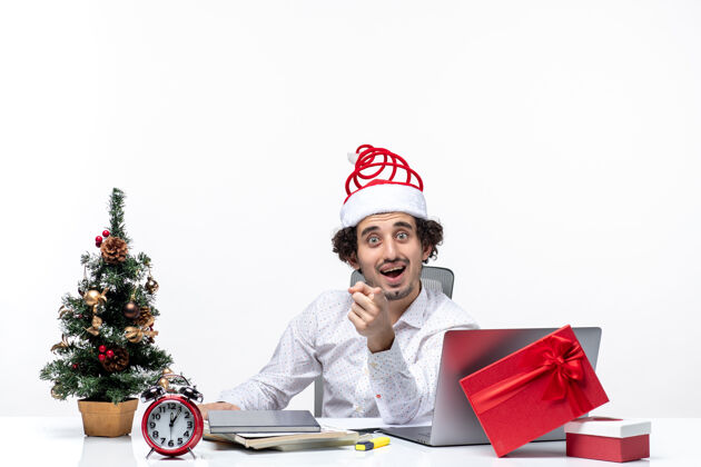 人新年心情惊喜地微笑着兴奋的年轻商人戴着圣诞老人的帽子在白色背景的办公室里询问一些事情圣诞老人笔记本电脑圣诞老人