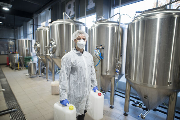 工程师在食品厂的生产线上 一个穿着白色防护服 戴着发网和面罩 拿着装有化学品的塑料罐的技术工人化学品工人
