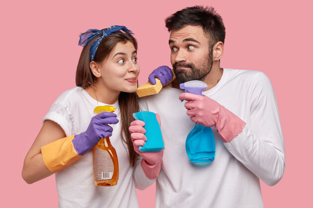 男性搞笑的欧洲夫妻拿着拖把和喷雾瓶 戴上橡胶防护手套清洁团队用品