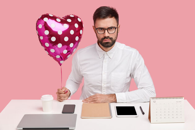 正式严肃的商人在工作场所接待女朋友的情人节 心形捧着气球 摆在桌面上衬衫咖啡专注