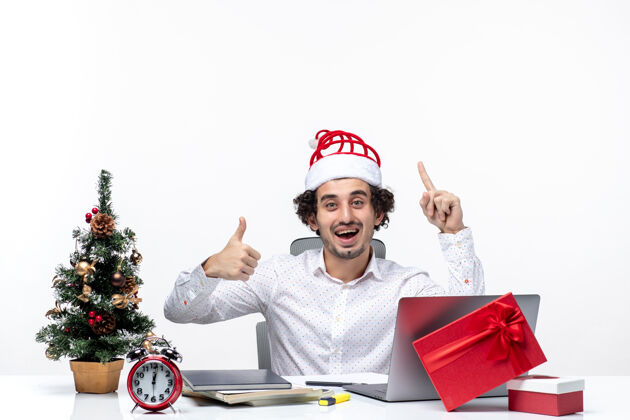 好快乐积极的年轻商人 戴着有趣的圣诞老人帽子 指着上方 在白色背景的办公室里做着“ok”的手势年轻圣诞老人手势
