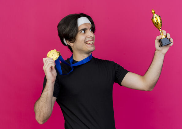 奖杯年轻的运动型男子穿着运动服 头上戴着金牌 脖子上展示着他的奖杯 看着它高兴又兴奋周围穿着兴奋