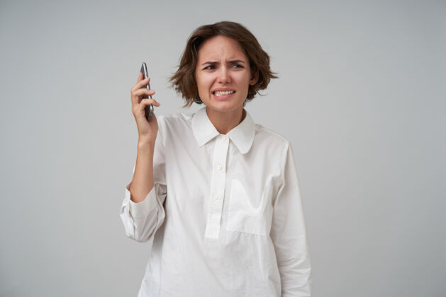 手机室内镜头：一位棕色短发的年轻女士在电话里说脏话 撅着嘴 扭着嘴 穿着正装站在一旁衣服撅嘴心情