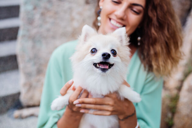 狗欧洲棕褐色卷曲女人的户外肖像抱着快乐的宠物狗波美拉尼亚斯皮茨顽皮肖像漂亮