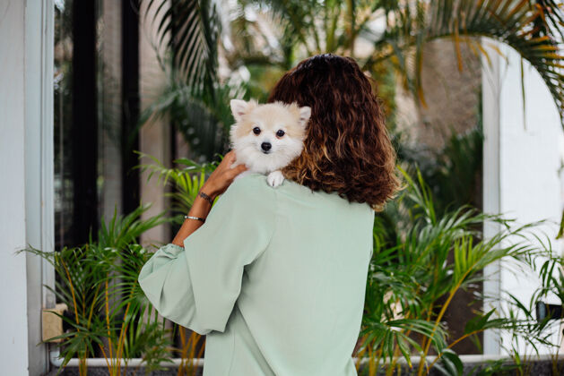 肖像欧洲棕褐色卷曲女人的户外肖像抱着快乐的宠物狗波美拉尼亚斯皮茨关怀主人狗