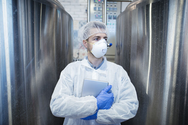 保护穿着防护服 手持药片的技术人员站在食品加工行业的金属容器旁手套制服专业