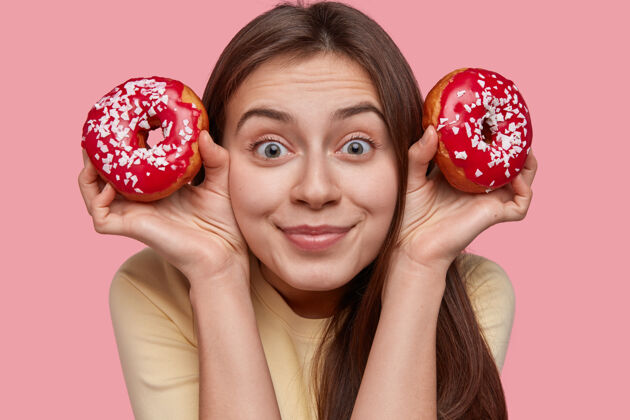 百吉饼令人高兴的可爱女性的特写镜头有着深色的头发 留着两个红色的甜甜圈和花洒女士个人甜食