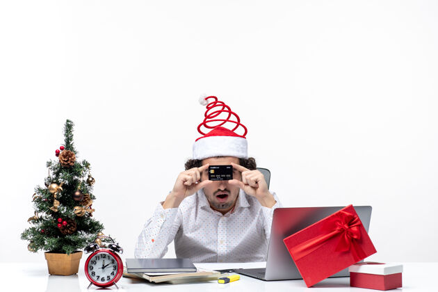 礼物带着圣诞老人帽 出示银行卡 在办公室的年轻商务人士的节日喜庆心情银行圣诞老人礼物