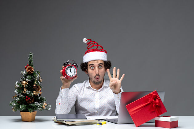 生活年轻人戴着圣诞老人的帽子 拿着钟 在黑暗的背景下 在办公室里展示了四个人 这让一位关心此事的商人大吃一惊年轻持有办公室