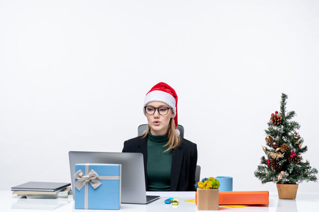 笔记本电脑新年的气氛与迷人的女人坐在一张桌子上 圣诞树和礼物的圣诞老人帽子白色背景电脑礼物桌子