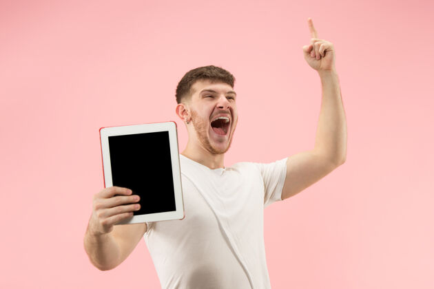 惊喜粉红色工作室里 一个微笑的男人指着笔记本电脑 空白屏幕被孤立电子男人男性