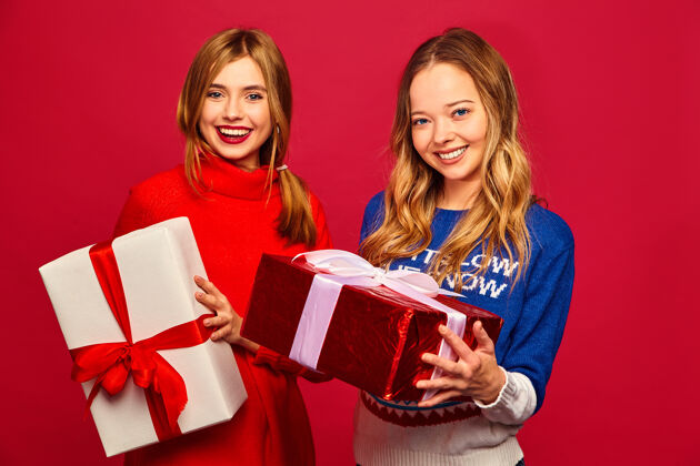 圣诞节两个微笑的漂亮女人穿着时髦的毛衣和大礼盒微笑姐妹人们