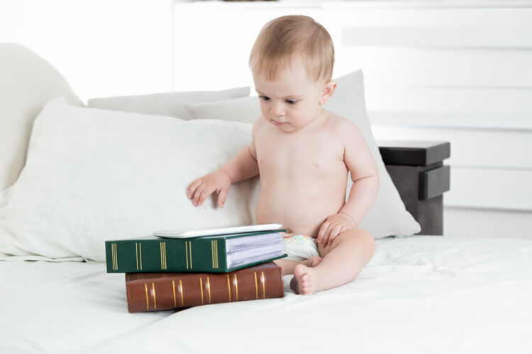 智能可爱的男婴用数字桌子躺在书堆上婴儿教育的概念小互联网天才