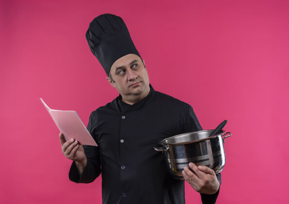 中年看着旁边穿着厨师制服的中年男厨师 手里拿着平底锅和笔记本 孤零零地贴在粉红色的墙上看制服拿着