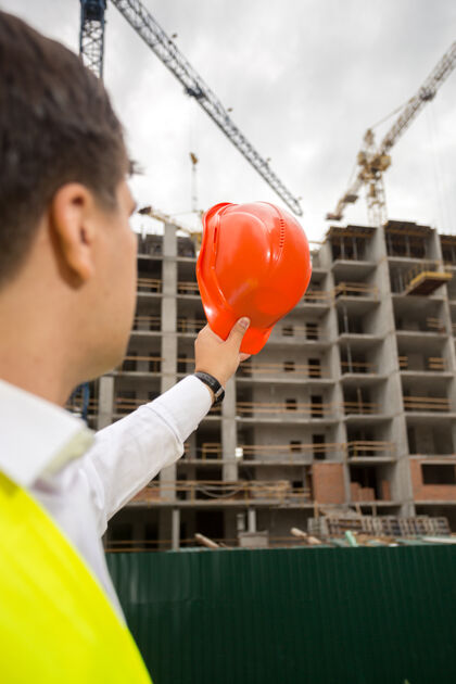 工程从后面看建筑工程师用红色安全帽指着建筑工地建造商建筑师夹克