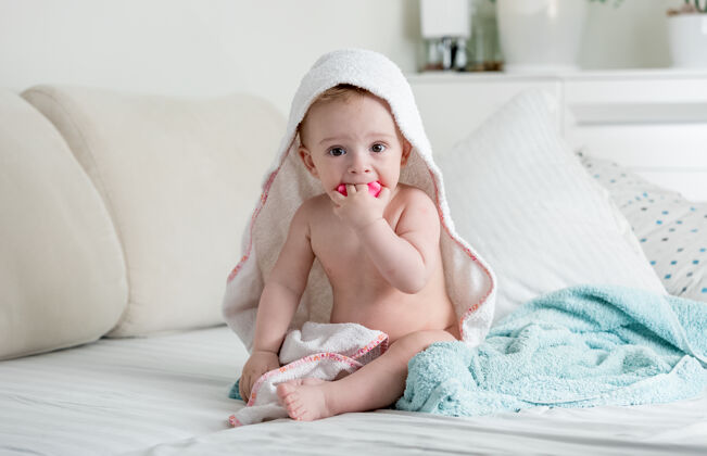 口腔可爱的9个月大的男孩坐在床上毛巾下玩具婴儿室内