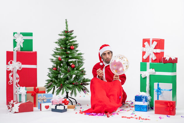 礼物圣诞气氛与年轻的圣诞老人坐在圣诞树和礼物在白色背景上不同的颜色坐着礼物不同