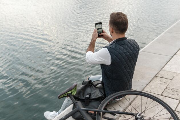人坐在自行车旁边给湖水拍照的男人运动的享受生态